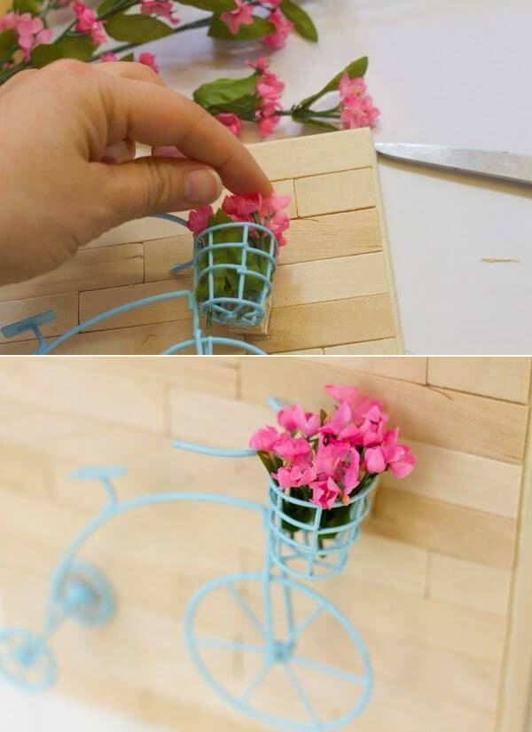 Dùng keo cố định mô hình xe đạp lên tấm gỗ và bỏ thêm hoa giả mini vào giỏ xe (Nguồn: Internet)