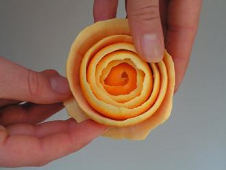 Cuộn vỏ cam theo hình xoắn ốc để tạo thành hình một bông hoa hồng và dùng tăm cố định lại phần đài (Nguồn: Internet)